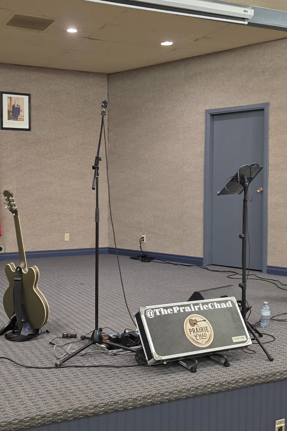 The Prairie Chad live rig on stage: guitar, mic, music stand, and branded case